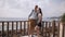 Young happy couple in love. Pair standing on wooden pier near sea or ocean and smiling to each other.