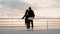 Young happy couple in love. Pair standing on wooden pier near sea or ocean and smiling to each other. People in black