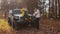 Young happy couple poses on camera with car and dog in autumn forest