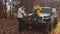 Young happy couple poses on camera with car and dog in autumn forest