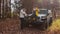 Young happy couple poses on camera with car and dog in autumn forest