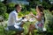 Young happy couple sits at the table and holds cups with tea in the garden