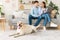 Young happy couple sitting on sofa with pc and dog