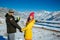 Young happy couple in snowy mountains with copy space. Guy and girl in bright clothes holding hands looking at camera and smiling