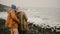 Young happy couple standing on the rocky shore of the sea in windy day. Man and woman exploring Iceland together.