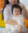 Young happy and cute Asian Chinese woman playing and holding sweet expressive baby girl sitting at holidays resort in mother and