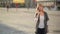 Young happy excited laughing woman talking on mobile phone, girl with red hair waves her hand at the street, city urban