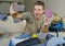 Young happy and excited man taking selfie portrait with mobile phone camera showing passport while packing travel suitcase and pre