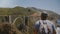 Young happy excited tourist man with backpack watching epic beautiful scenery of Bixby Canyon bridge, walking away.