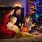 Young happy family of four unwrapping Christmas gifts by a fireplace