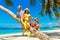Young happy family-mom, dad, daughter and son having fun on a coconut tree on a sandy tropical beach. The concept of travel and