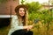 Young happy farmer woman in straw hat sitting in garden taking care of her plants and harvest. Female smiling in her