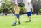 Young happy father and excited 7 or 8 years old son playing together soccer football on city park garden running on grass kicking