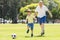 Young happy father and excited little 7 or 8 years old son playing together soccer football on city park garden running on grass k