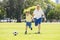 Young happy father and excited little 7 or 8 years old son playing together soccer football on city park garden running on grass k