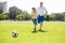 Young happy father and excited little 7 or 8 years old son playing together soccer football on city park garden running on grass k