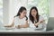 Young happy friends working in office. Two beautiful Asian woman sitting in office with laptop and document paper chart on desk.