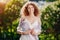 Young happy girl in the bushes of blooming lilac. Fashion portrait smiling curly woman against lilac in blossom. Positive model in