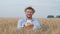 Young happy grain grower, handsome man in straw hat gives you at camera tasty baked bread and smiles standing in field