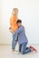 Young happy guy is kneeling and hugging his beloved woman thinking of another man posing on a white background. Unequal