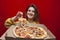 Young happy hungry girl eats fresh pizza from a box on a colored background, a student takes a slice of pizza from a box