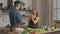 Young happy husband hug smiling wife cutting vegetable for salad in kitchen, affectionate couple cooking dancing together. Prepare