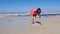 Young happy lady draws pictures on the sea beach sand. Strong stormy waves hitting the seashore. Wind blows. Slow motion