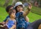 Young happy loving Asian Korean family with parents and sweet baby daughter at city park together with father taking selfie pic