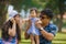 Young happy loving Asian Korean parents couple enjoying together sweet daughter baby girl sitting on grass at green city park in