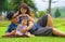 Young happy loving Asian Korean parents couple enjoying together sweet daughter baby girl sitting on grass at green city park in