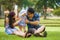 Young happy loving Asian Korean parents couple enjoying together sweet daughter baby girl sitting on grass at green city park in
