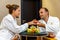 Young happy loving Caucasian couple of man and woman in white bathrobes talking after spa on honeymoon. Different fruits lying on