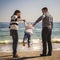 Young happy loving family with small kid in the middle, having fun at beach together near the ocean, holding arms, happy lifestyle