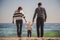 Young happy loving family with small kid in the middle, walking at beach together near the ocean, holding arms, happy lifestyle fa