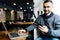 Young happy man smiling and holding a smartphone sitting with laptop in cafe. Portrait man reading a message with smartphone in ca