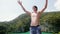 Young happy man in sunglasses stands on view point next to azure lagoon and smiles raises his arms forward at the sea