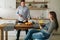 Young happy married couple in kitchen. Man is standing by kitchen table and preparing breakfast. Pregnant woman sits