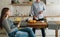 Young happy married couple in kitchen. Man is standing by kitchen table and preparing breakfast. Pregnant woman sits