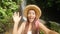 Young Happy Mixed Race Tourist Blogger Girl in White Dress and Straw Hat Making Selfie Video Using Mobile Phone at Amazing Wild