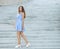 Young happy playful woman in light striped white blue dress posing at concrete stairway outdoor