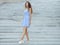 Young happy playful woman in light striped white blue dress posing at concrete stairway outdoor