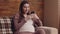 Young happy pregnant lady chatting on cellphone, reading message and laughing, resting on couch at home, slow motion