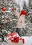 Young happy pretty woman in stylish winter clothing decorates outdoor Christmas New Year tree fir with red balls