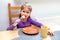 Young happy primary school european girl eating her food by herself, grabbing a last bite on a fork, empty plate and a mug