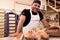 Young happy and smiling bread baker posing proud with fresh traditional bread in bread making factory. concept of traditional