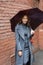 Young happy smiling pretty girl in gray coat and turtleneck poses with umbrella