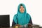 Young happy and successful Muslim student woman in traditional Islam hijab head scarf working on desk studying with laptop