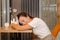 Young, happy, tired european girl with brown hair sits in cafe at wooden table with flower, lying on a white laptop