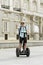 Young happy tourist man with backpack riding city tour segway driving happy and excited visiting Madrid palace