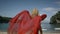 Young happy woman with curly blonde hair in elegant long red dress walking on beach in famous place